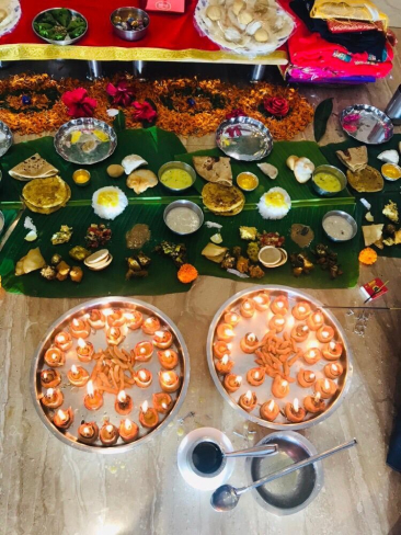 In the foreground are Diyas (oil lamps), and in the background, traditional Indian sweets and offerings placed on banana leaves